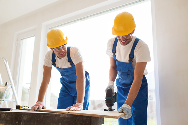 Two construction workers in hard hats cutting wood indoors